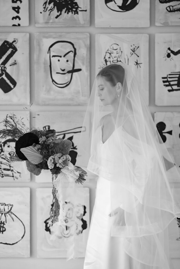 emotional black and white photo of a veiled bride with artwork behind her