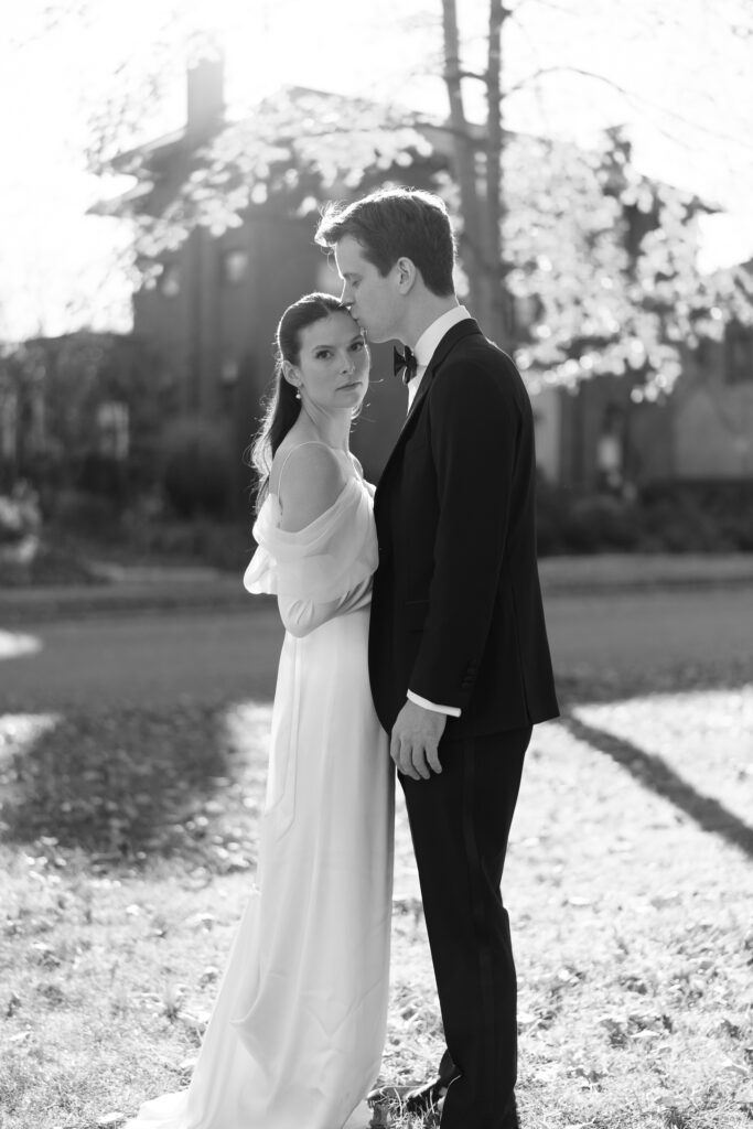 minimalistic black and white portrait of the bride looking at the camera and the groom kissing the bride's temple