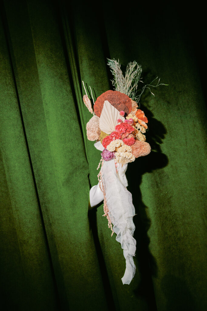 Bride holding a bespoke handmade bouquet through a green velvet curtain.