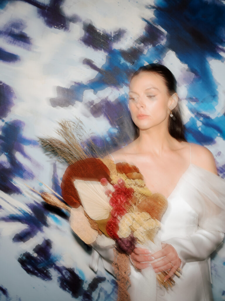 direct flash motion blur photo of a bride holding her red and tan bouquet in front of a large blue and white painting