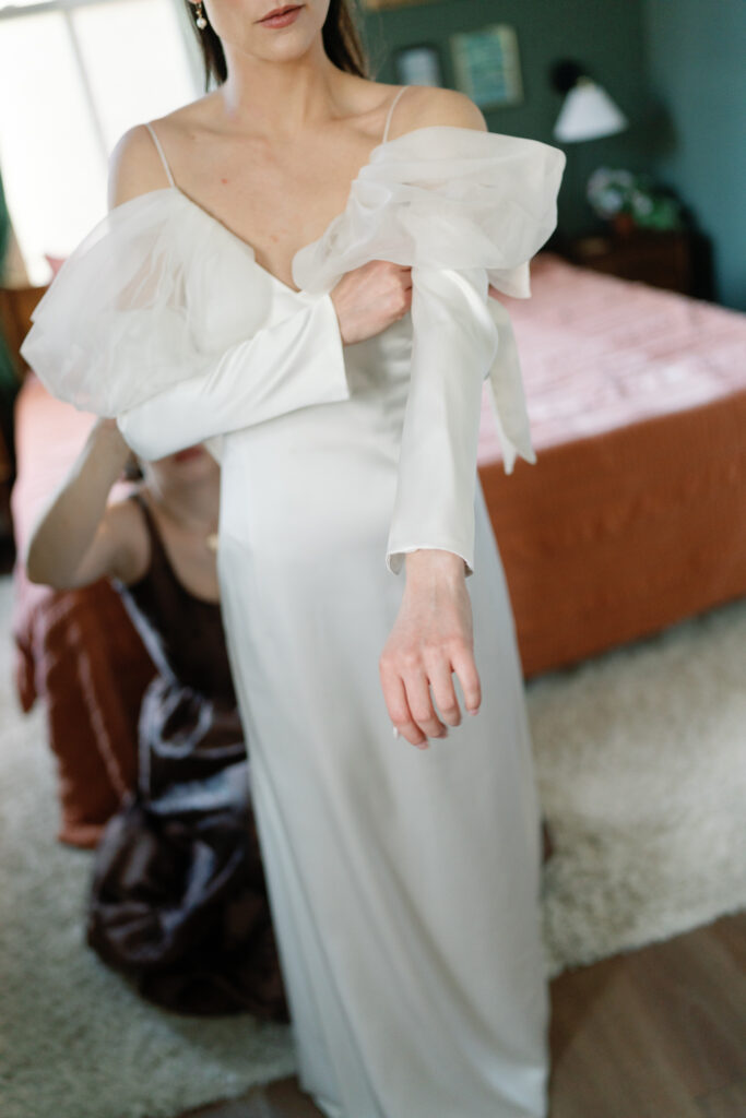 bride adjusting the sleeve on her dress with beautiful window light illuminating the subject