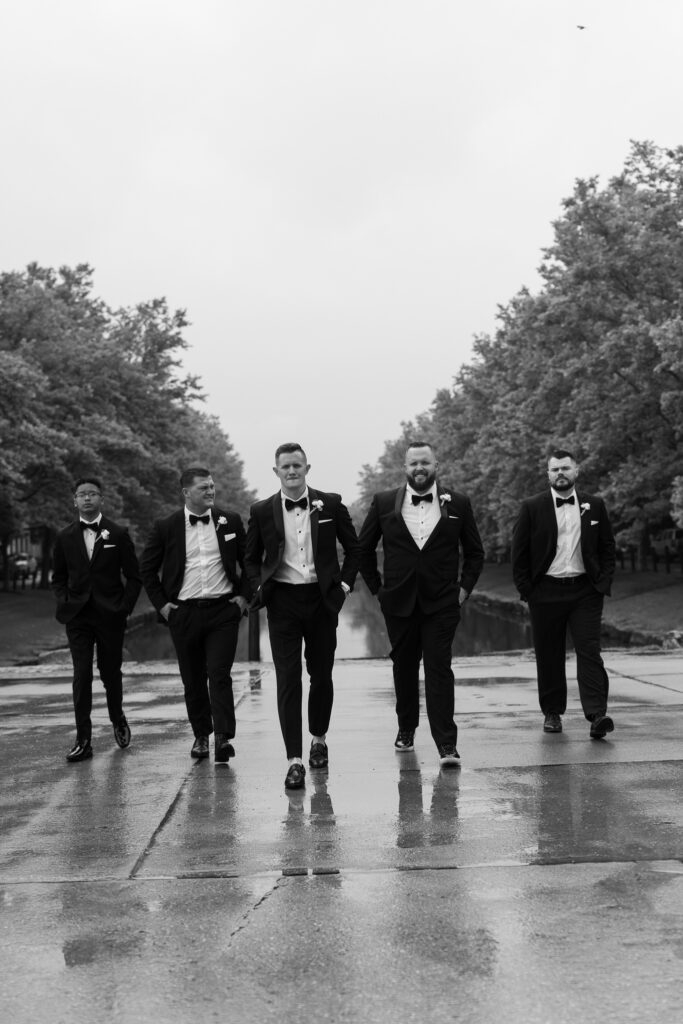 Groom laughing with groomsmen in tuxedos by waterway at The Marquee at New Town in St. Louis