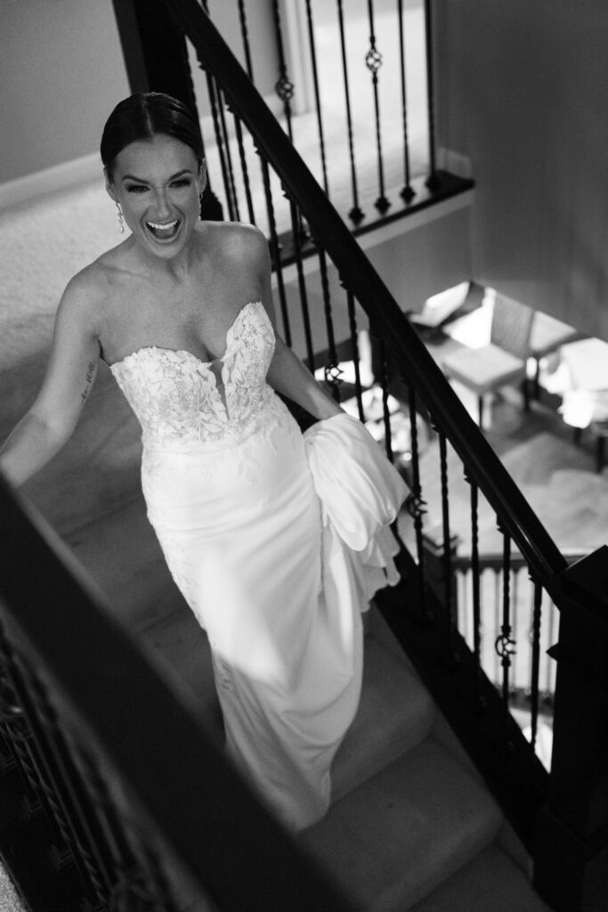 Bride in lace dress laughing while walking downstairs before ceremony at The Marquee at New Town