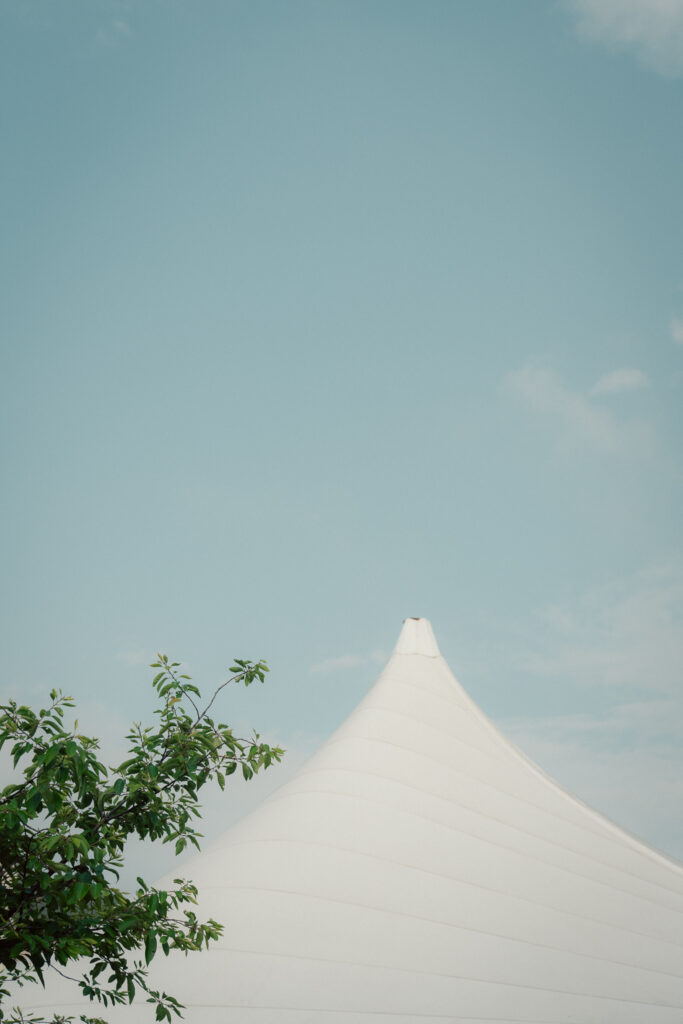 White sailcloth wedding tent peak with blue sky and greenery at The Marquee at New Town