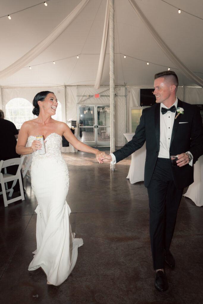 Bride and groom laughing and holding hands during wedding reception entrance under tent at The Marquee at New Town